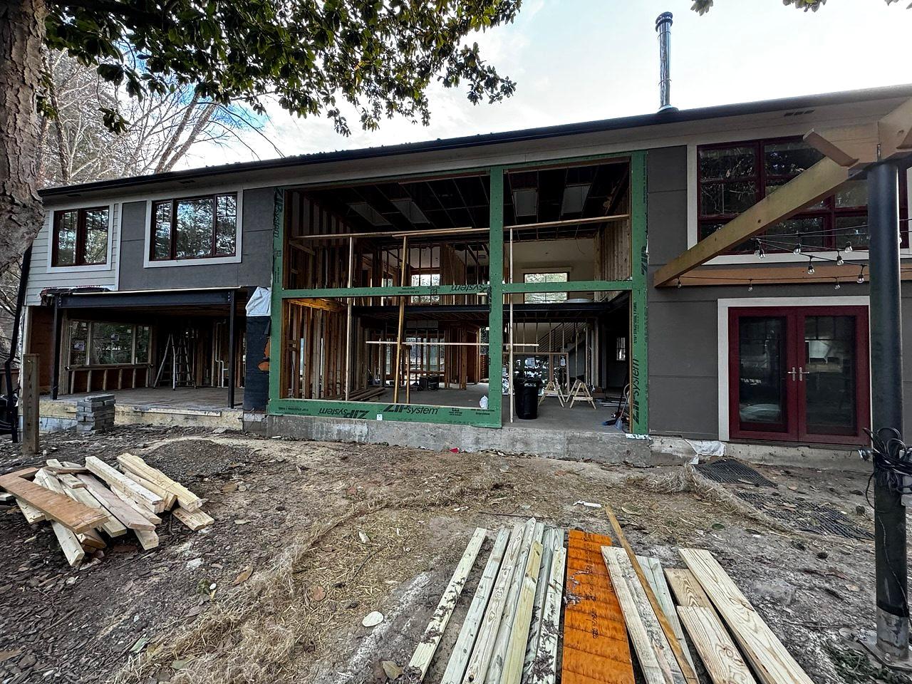 Rear wall of the house opened up for a new wall of glass, lumber staged in the yard