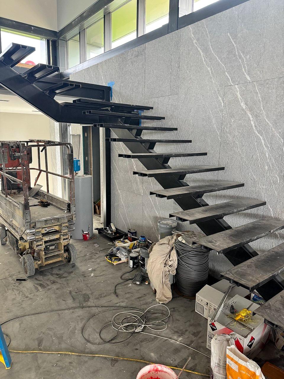 Floating steel stair against a large-format stone wall, mid-install