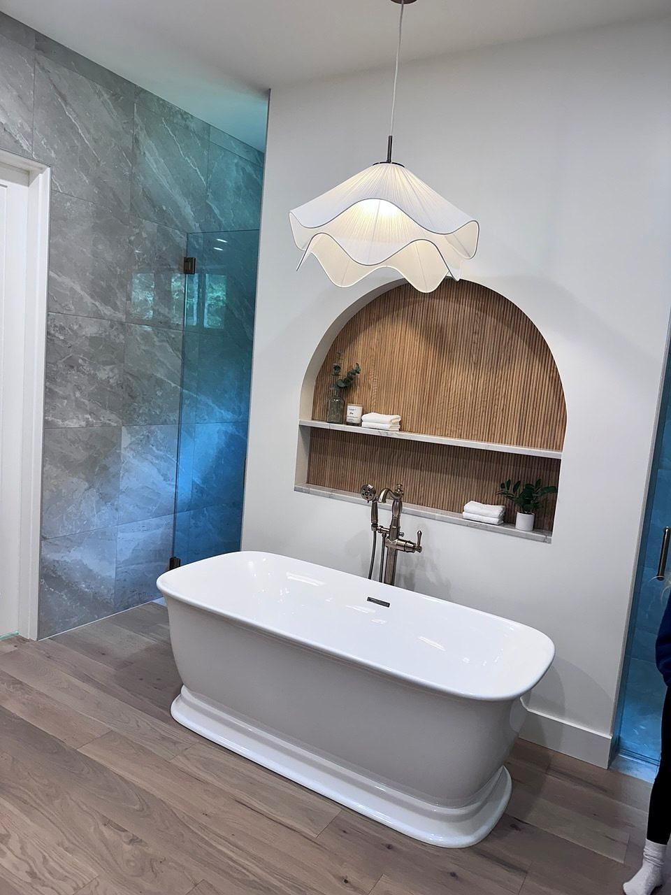 Freestanding tub beneath an arched wood-lined niche and a sculptural pendant
