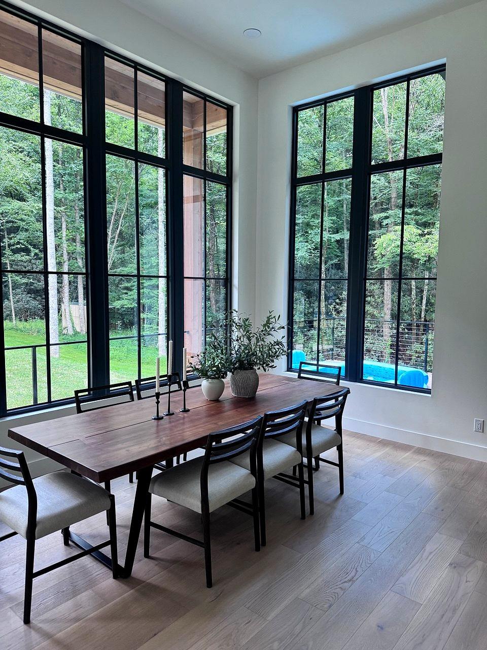 Double-height dining room framed by floor-to-ceiling black steel windows onto the woods