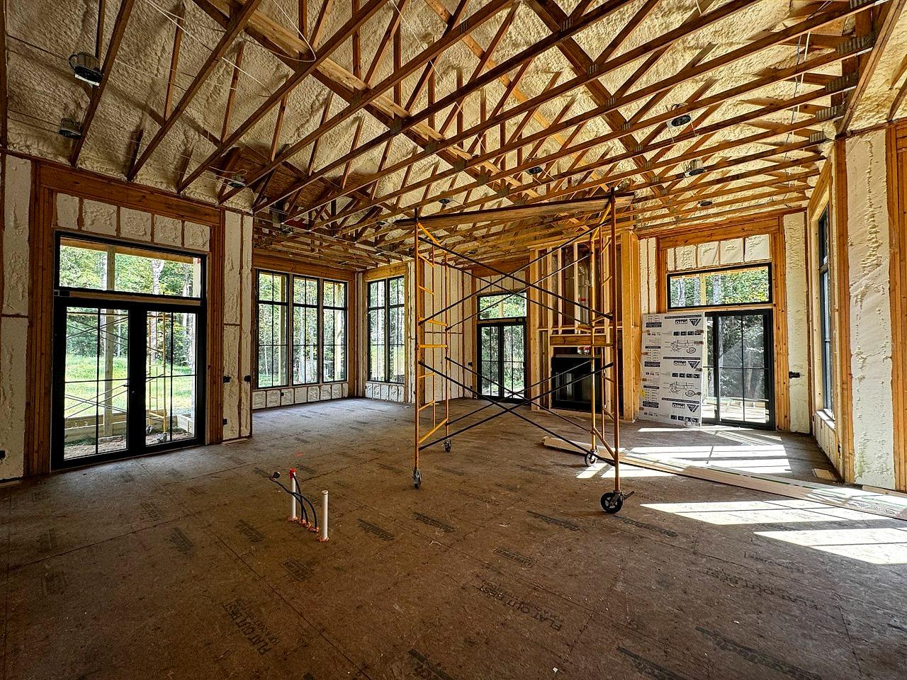 Great room under construction — spray foam, exposed trusses and window openings on every wall