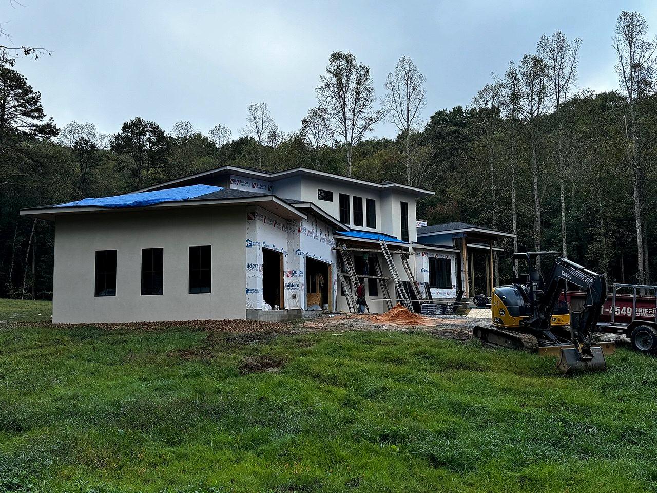Stucco shell of the South Asheville home on its wooded lot, excavator on site