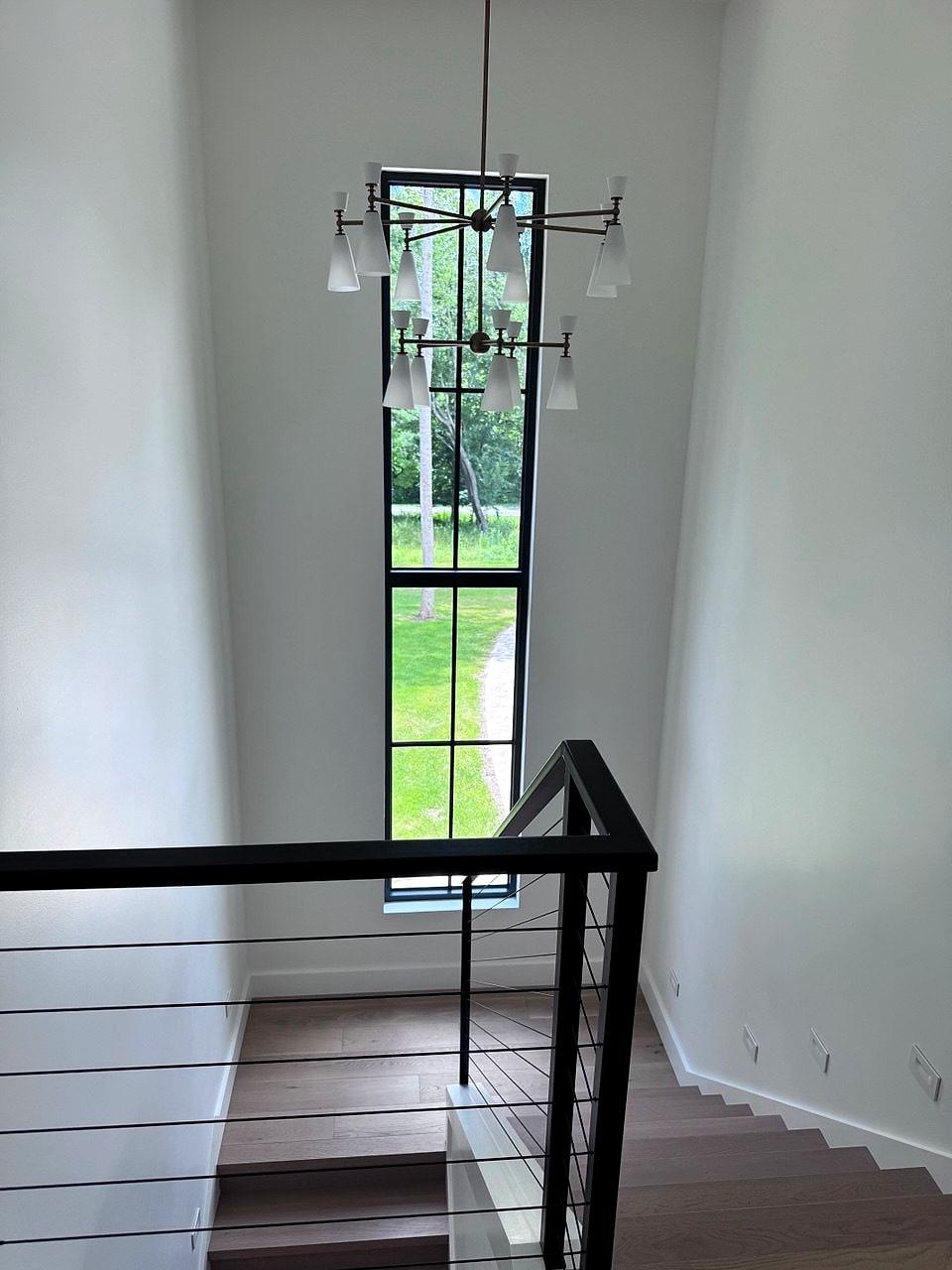 Stairwell with a tall slot window, cable railing and a linear chandelier