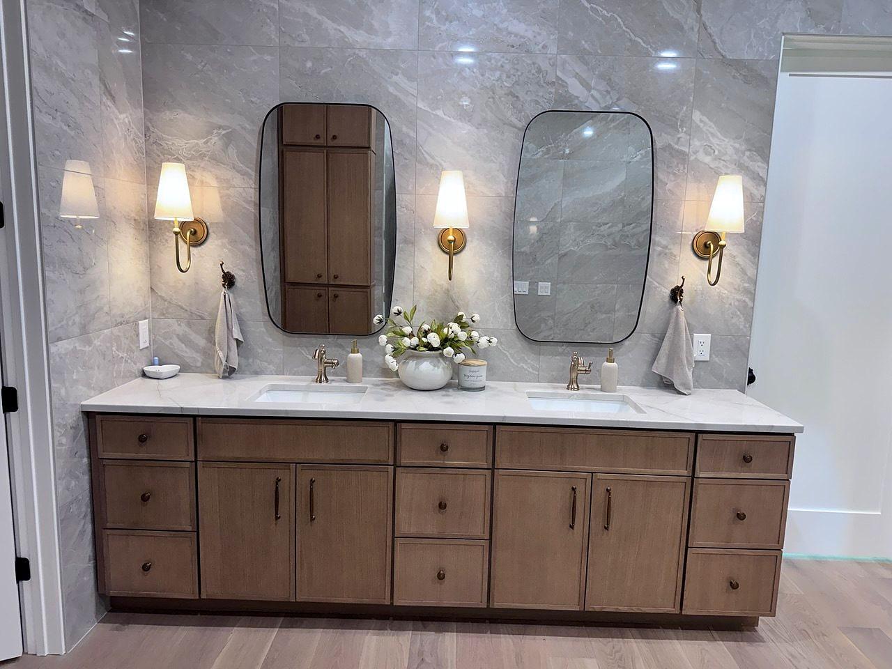 Double vanity with large-format marble tile, brass sconces and pill-shaped mirrors