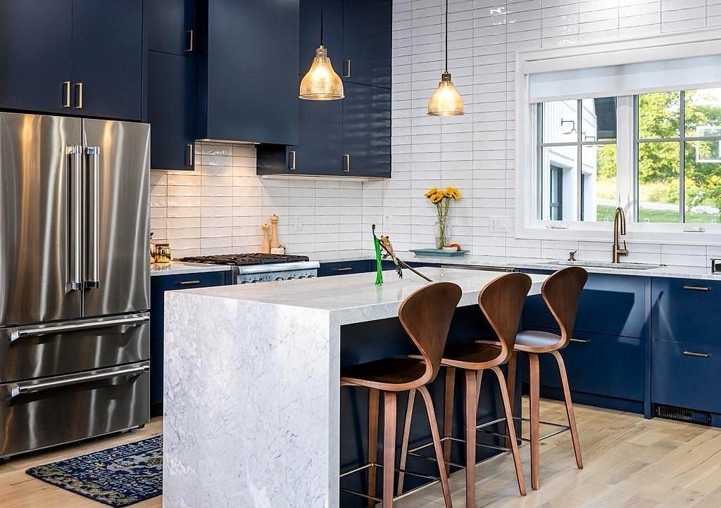 Navy kitchen with a marble waterfall island, walnut stools and white subway tile