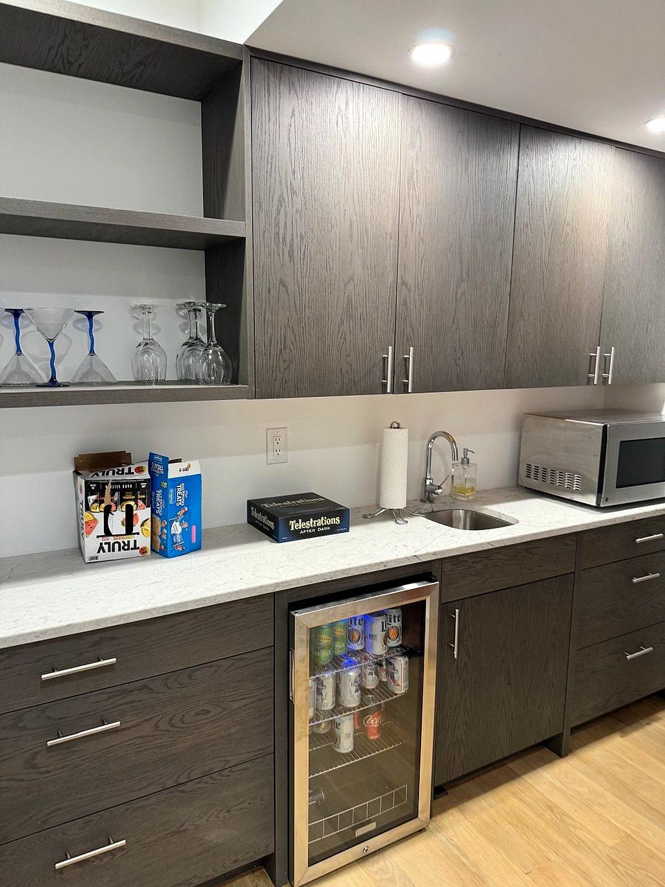 Wet bar with dark oak cabinetry, open shelving and a beverage fridge
