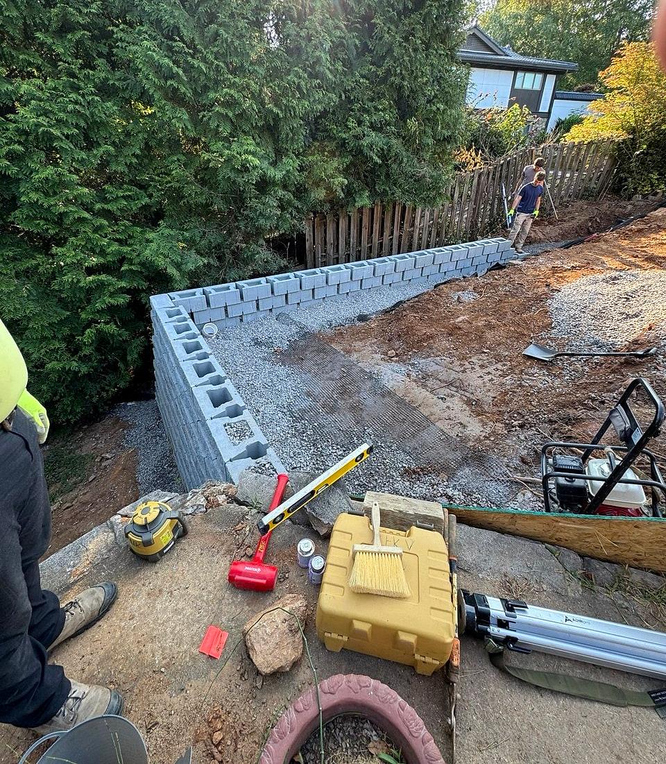 Block retaining wall going up along the property line, with layout tools on the ground